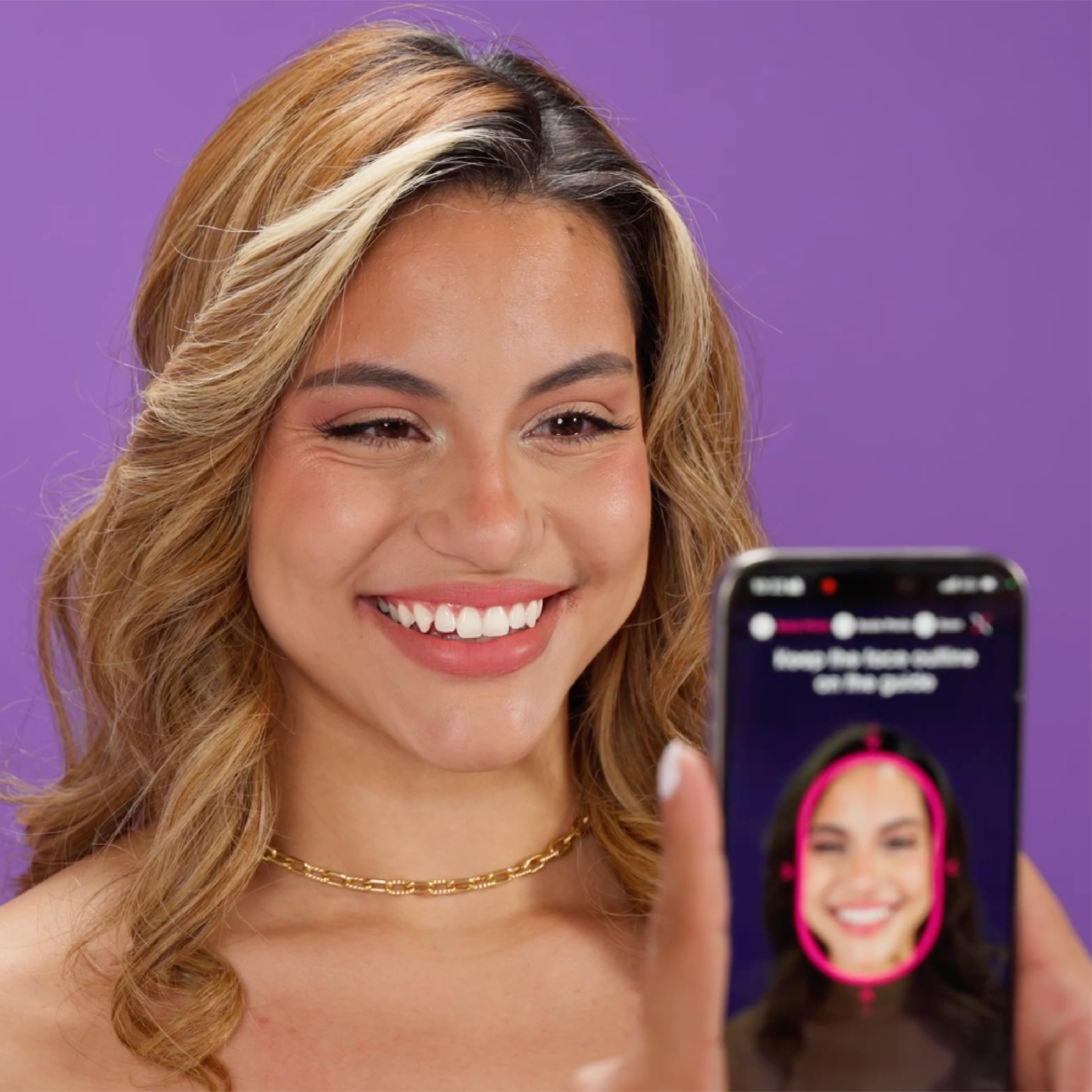 A person smiling and holding a phone with their own smiling image on the screen
